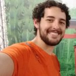 Imagem quadrada de Paulo Alarcón, posando em uma selfie, com o braço direito estendido, sorrindo e vestido com uma camiseta de cor laranja.